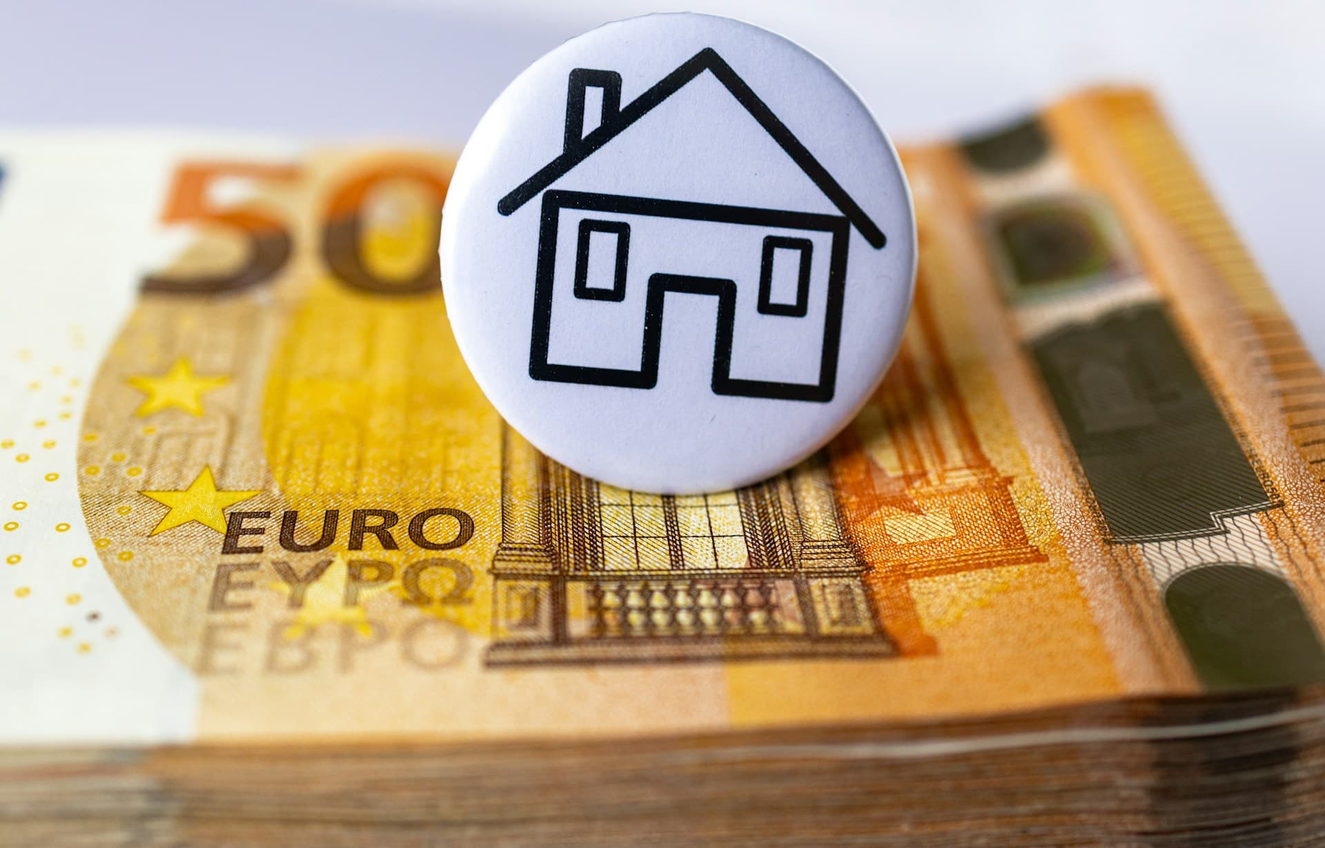 A house icon on a pile of euro bills representing property purchase taxes and fees in Madrid.